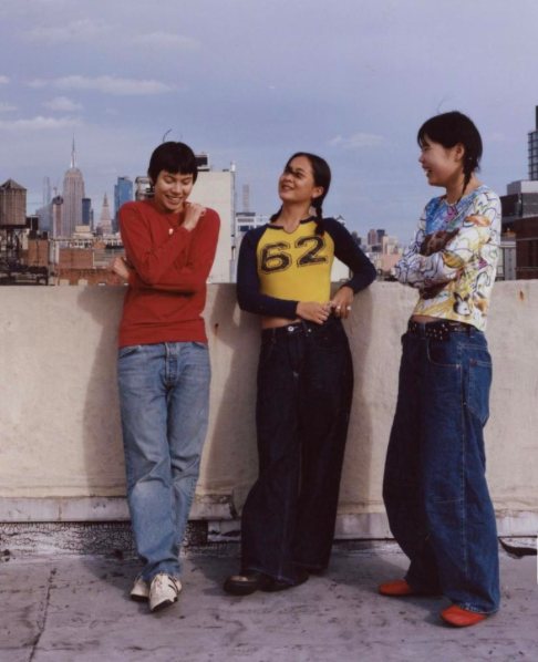 Three friends laughing on a rooftop in secondhand outfits